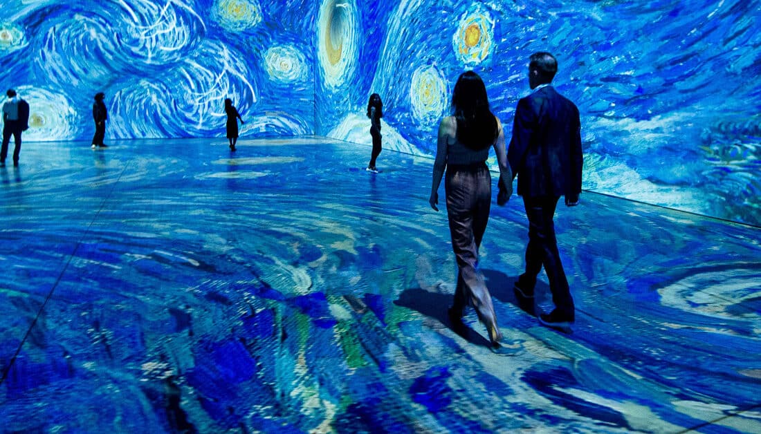 A couple holding hands and walking through Starry Night at Beyond Van Gogh